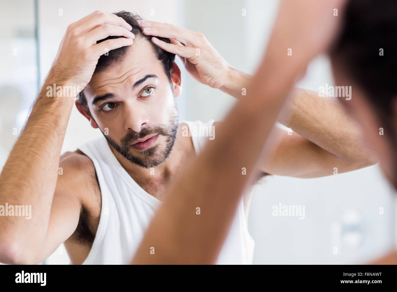 Concentrate l uomo guardando i suoi capelli in specchio Foto Stock