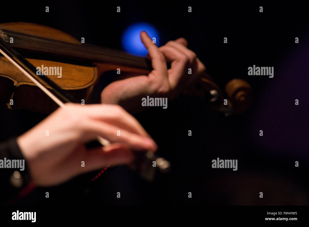 Le mani la riproduzione di un violino con un blu splendente di Spotlight in background Foto Stock
