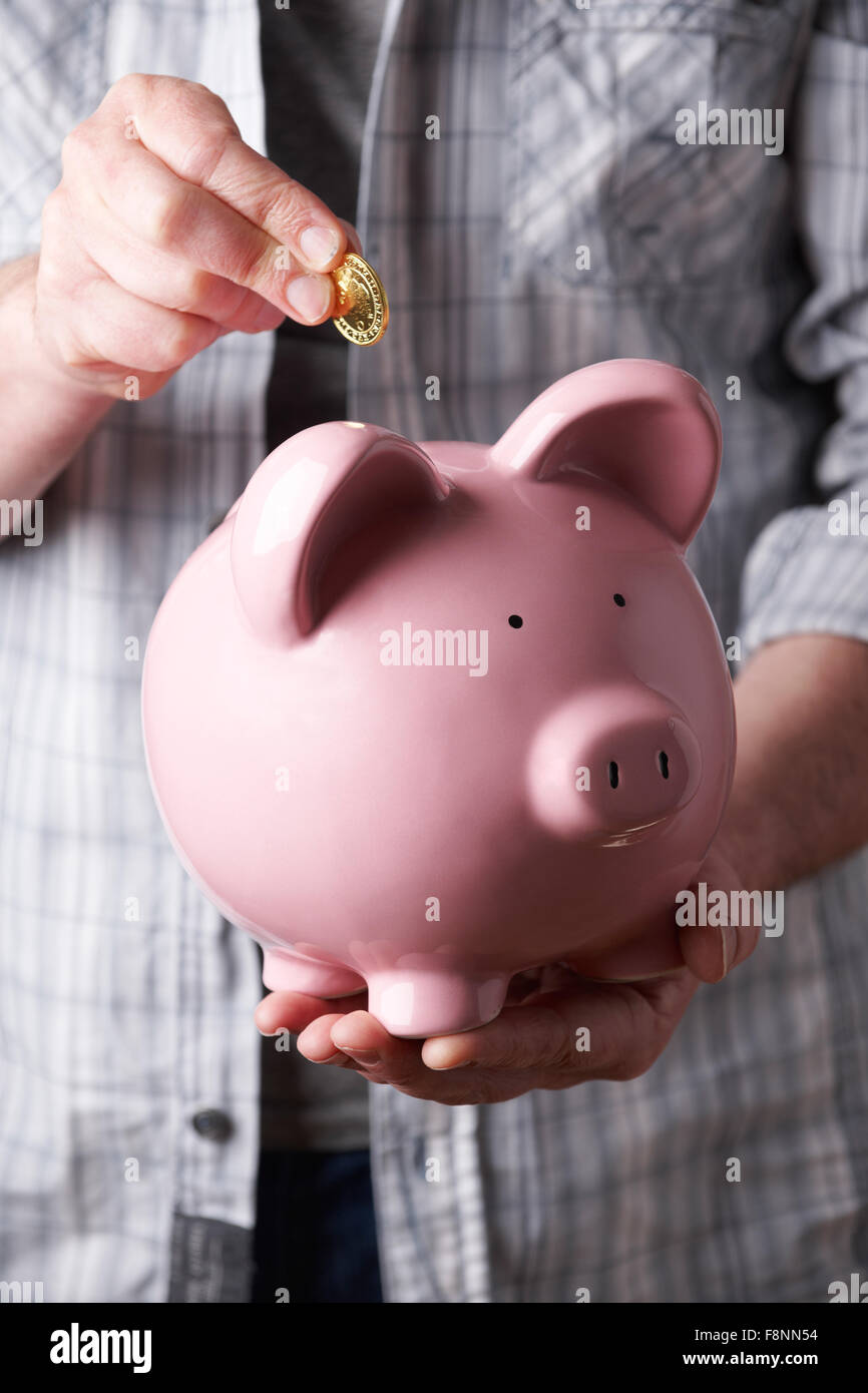 Uomo di mettere moneta nella grande Salvadanaio Foto Stock