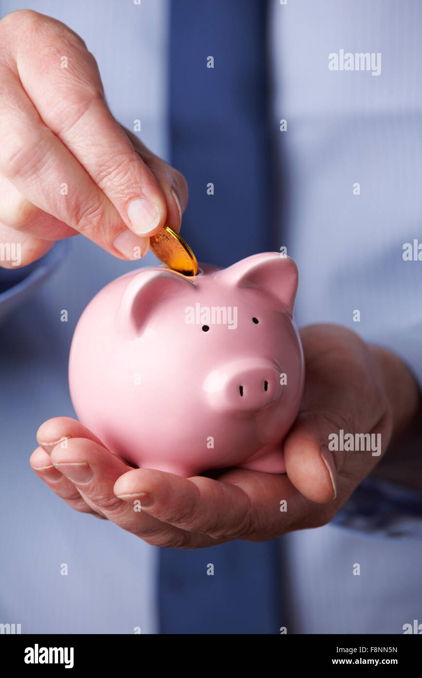 Imprenditore mettendo moneta nel salvadanaio Foto Stock