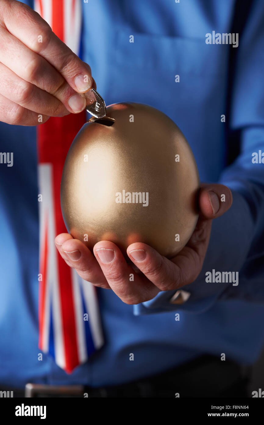 Imprenditore in Unione Jack Tie mettendo in moneta a forma di uovo banca di risparmio Foto Stock
