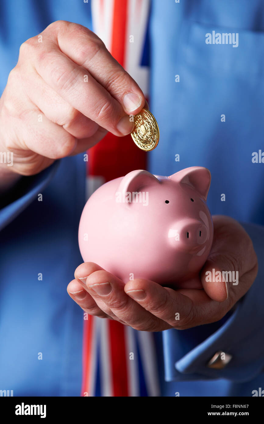 Imprenditore britannico in Unione Jack Tie mettendo moneta nel salvadanaio Foto Stock