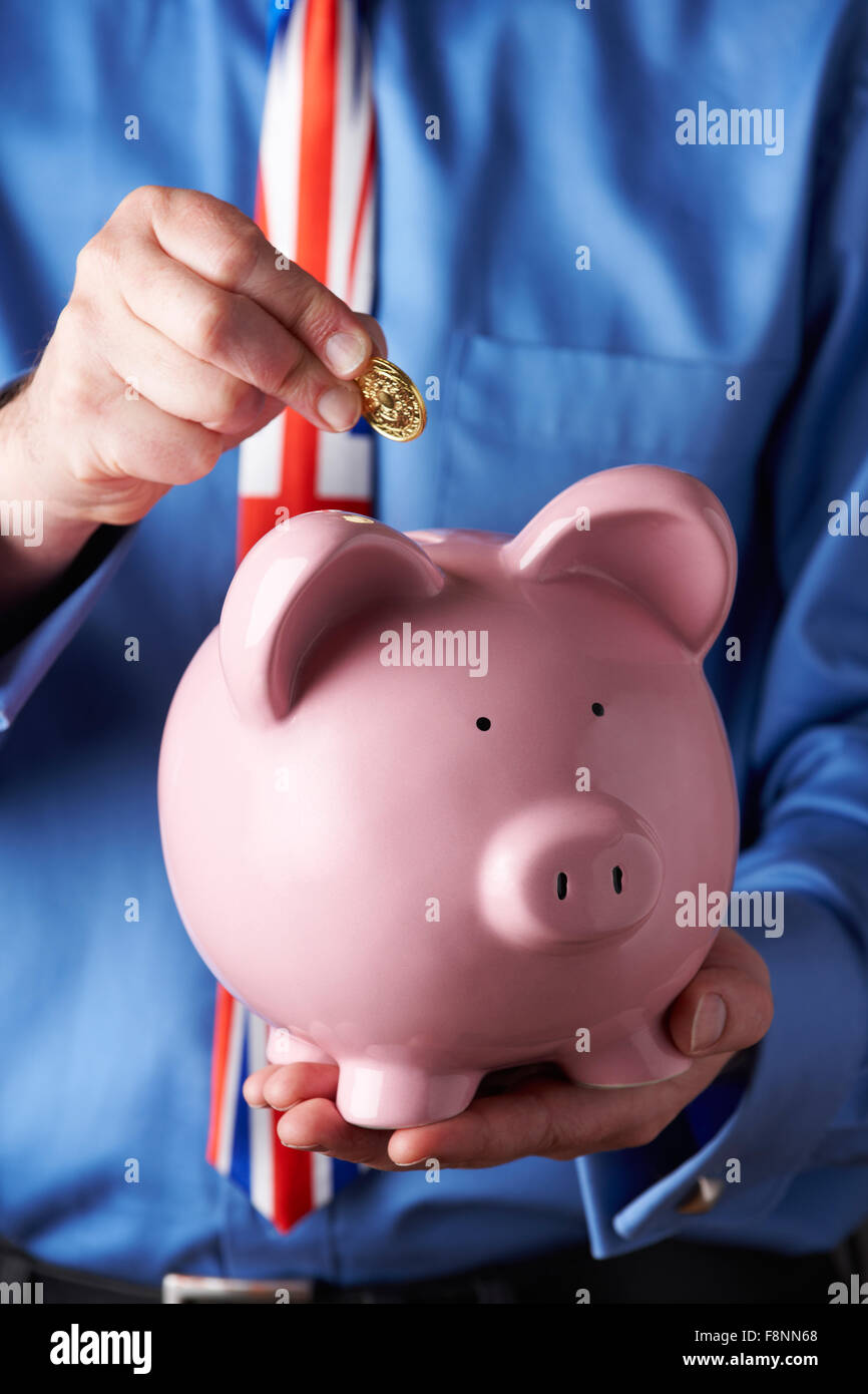 Imprenditore indossando Unione Jack Tie mettendo moneta nel salvadanaio Foto Stock