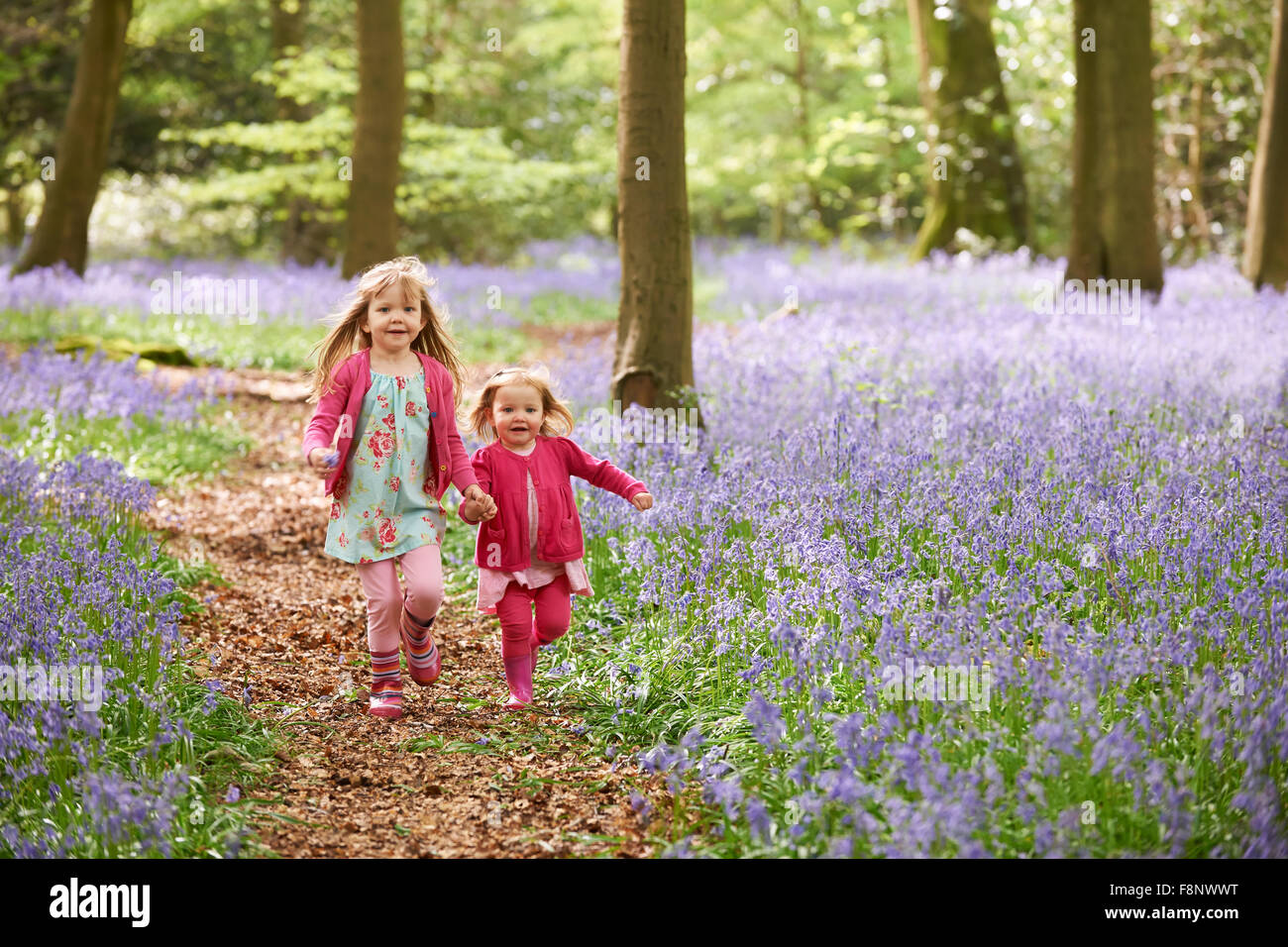 Due ragazze in esecuzione attraverso la ferrovia Bluebell bosco insieme Foto Stock