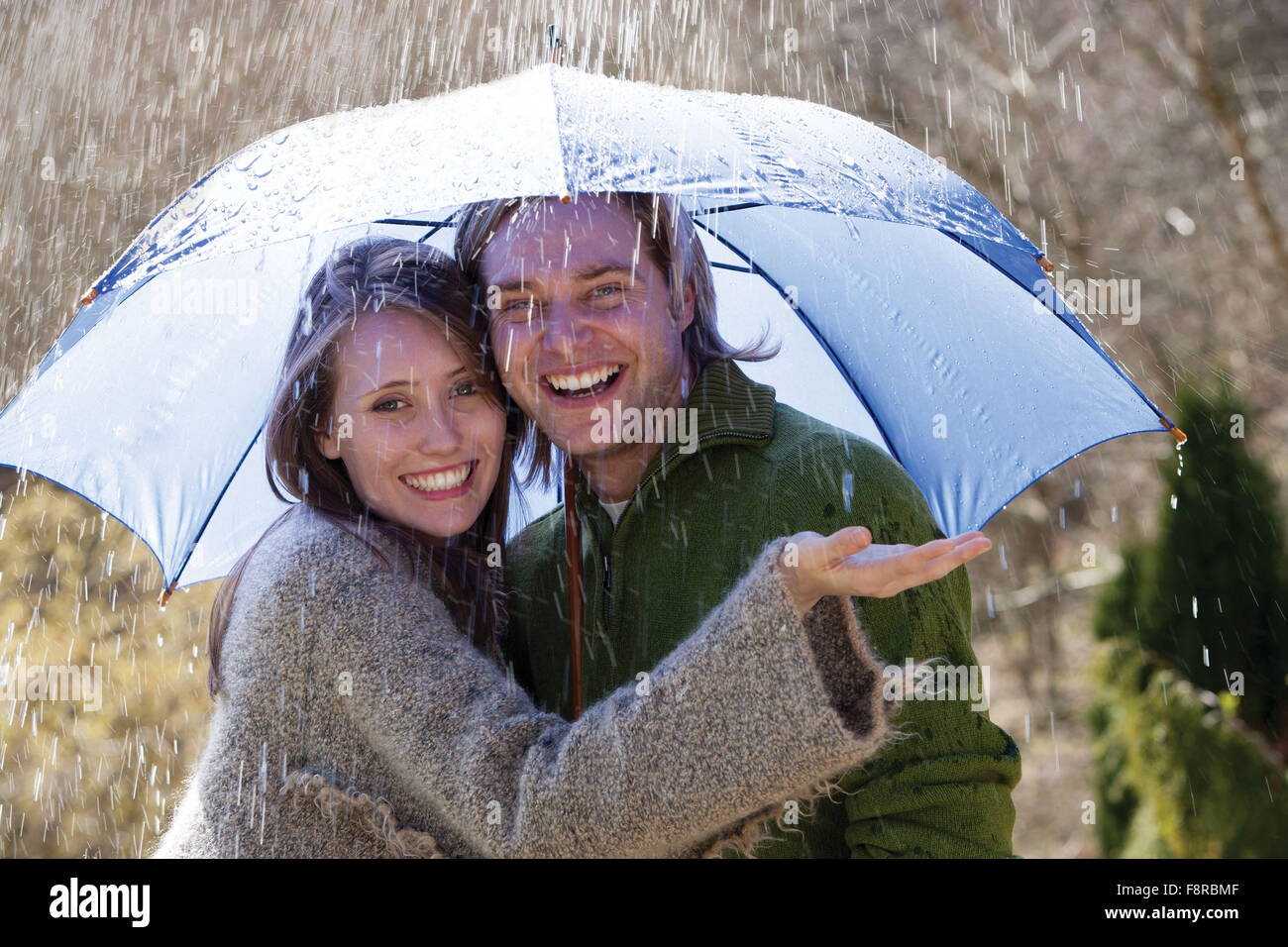 Coppia giovane godendo la pioggia sotto un ombrello Foto Stock