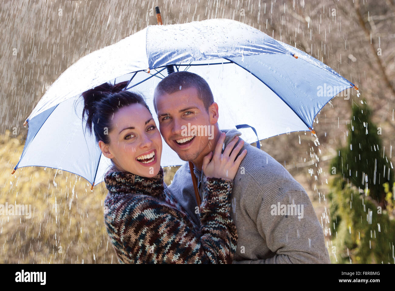 Coppia giovane ridendo sotto la pioggia sotto un ombrello Foto Stock