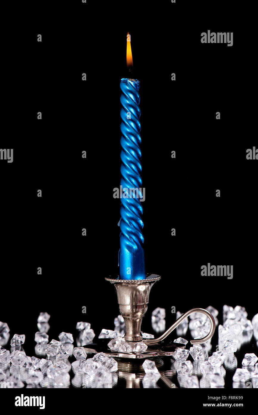 Argento candelabro con una candela blu sorge accanto ad una moltitudine di pietre di cristallo a specchio nella parte anteriore di un nero backgroun Foto Stock