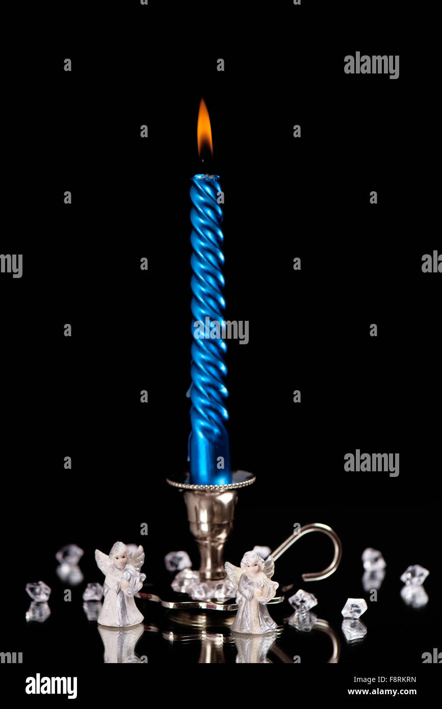 Argento candelabro con una candela blu sorge accanto ad una moltitudine di pietre di cristallo a specchio nella parte anteriore di un nero backgroun Foto Stock