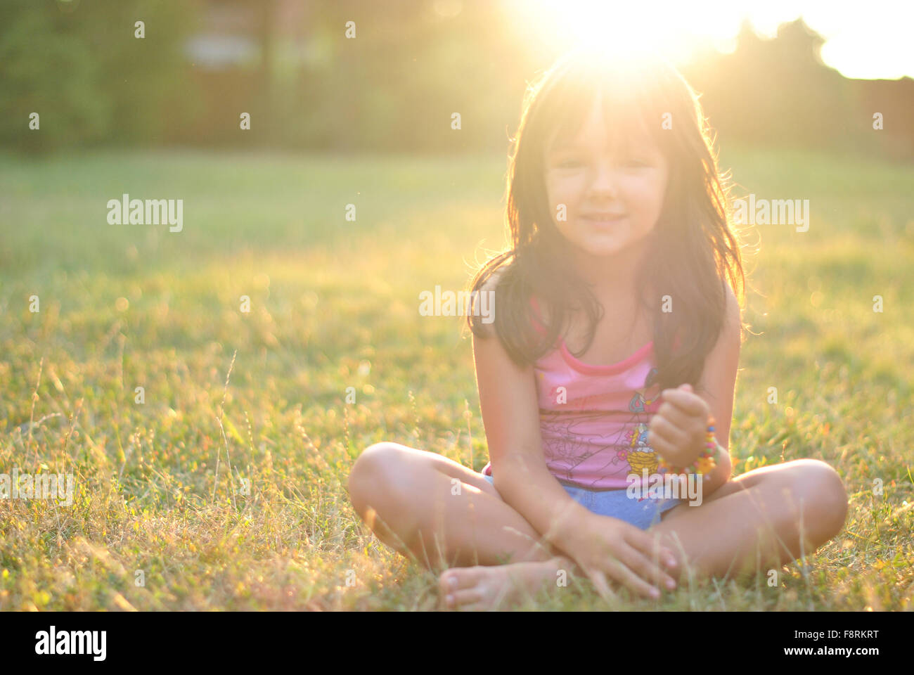 Ritratto di una ragazza seduta zampe trasversale sull'erba con il sole che splende su i suoi capelli Foto Stock