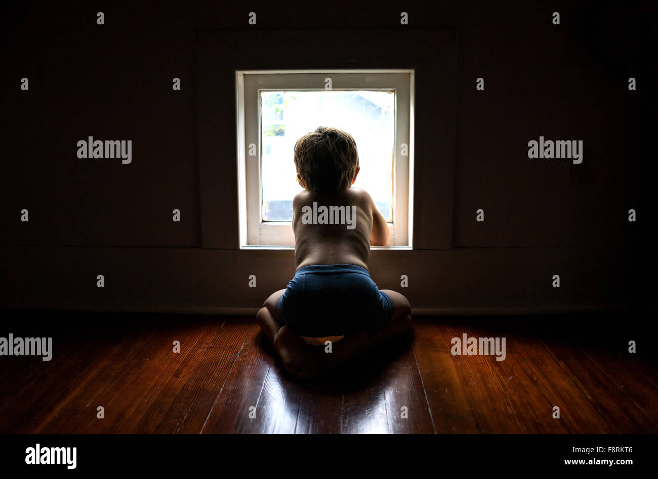 Ragazzo seduto sul pavimento guardando fuori della finestra Foto Stock