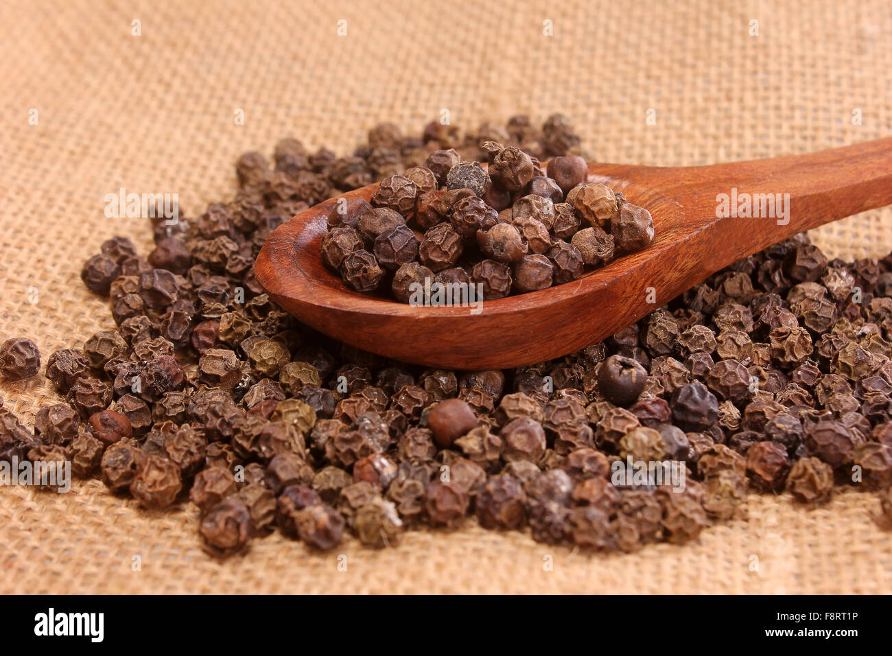 Peperoni nero sul cucchiaio di legno Foto Stock