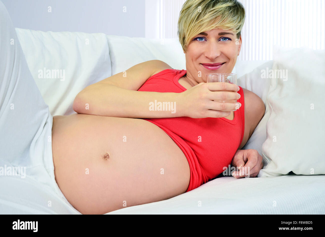 Donna incinta azienda glas di acqua e sorridente Foto Stock