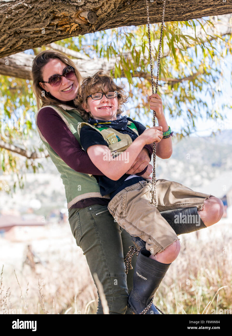 Attraente madre aiuta i giovani figlio su swing corda appesa da ranch tree Foto Stock