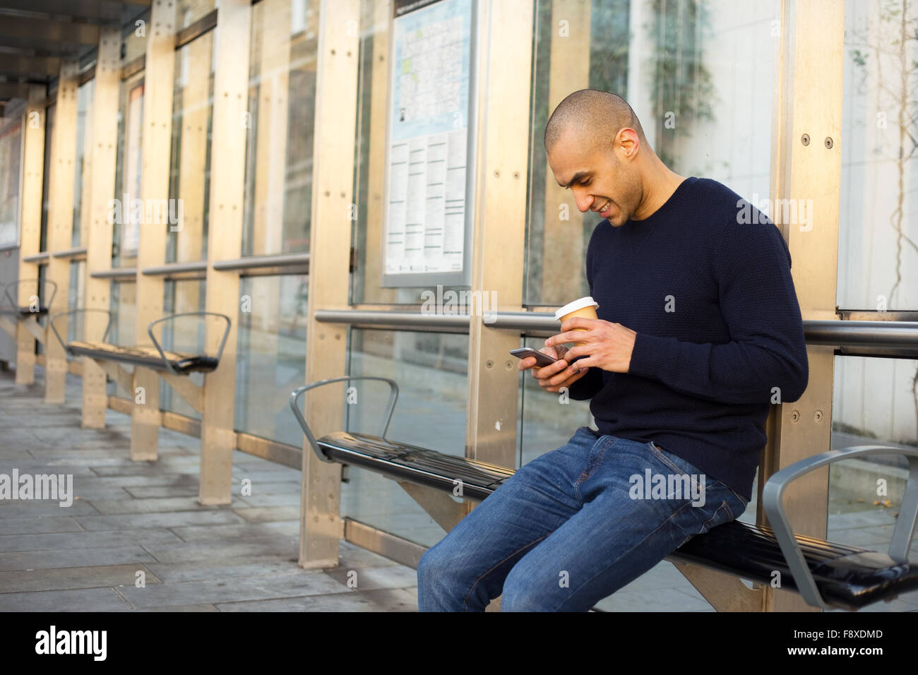 Giovane uomo presso la fermata del bus con un caffè e telefono Foto Stock