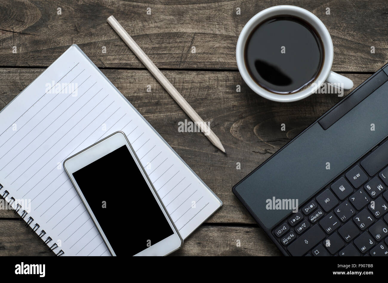 Blank notepad, telefono portatile e la tazza di caffè su office tavolo in legno Foto Stock