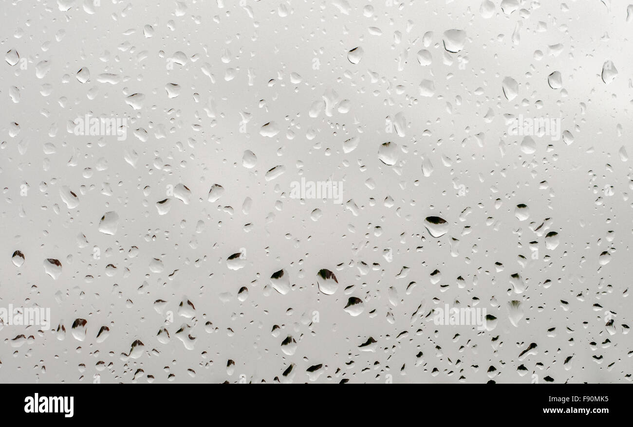 Gocce di pioggia su un vetro di finestra durante una fredda e umida giornata invernale Foto Stock