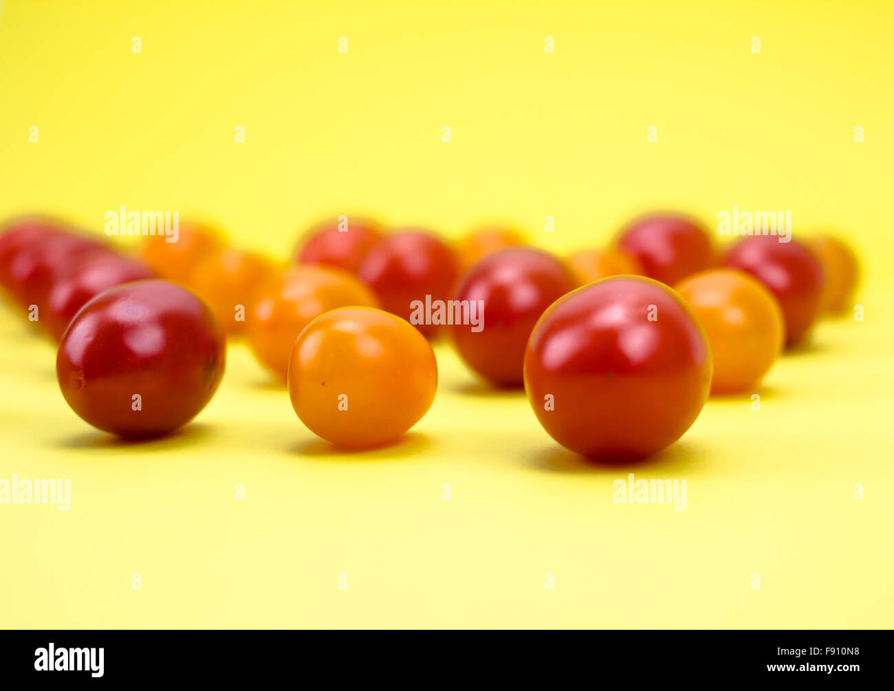 Rosso e arancio i pomodori ciliegia su sfondo giallo Foto Stock