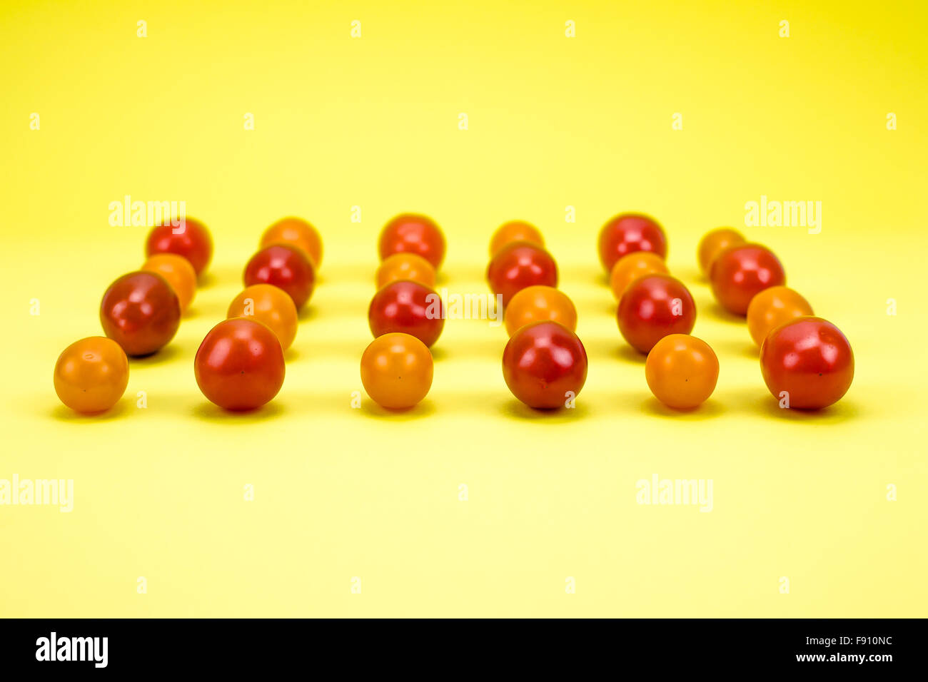 Rosso e arancio i pomodori ciliegia su sfondo giallo Foto Stock