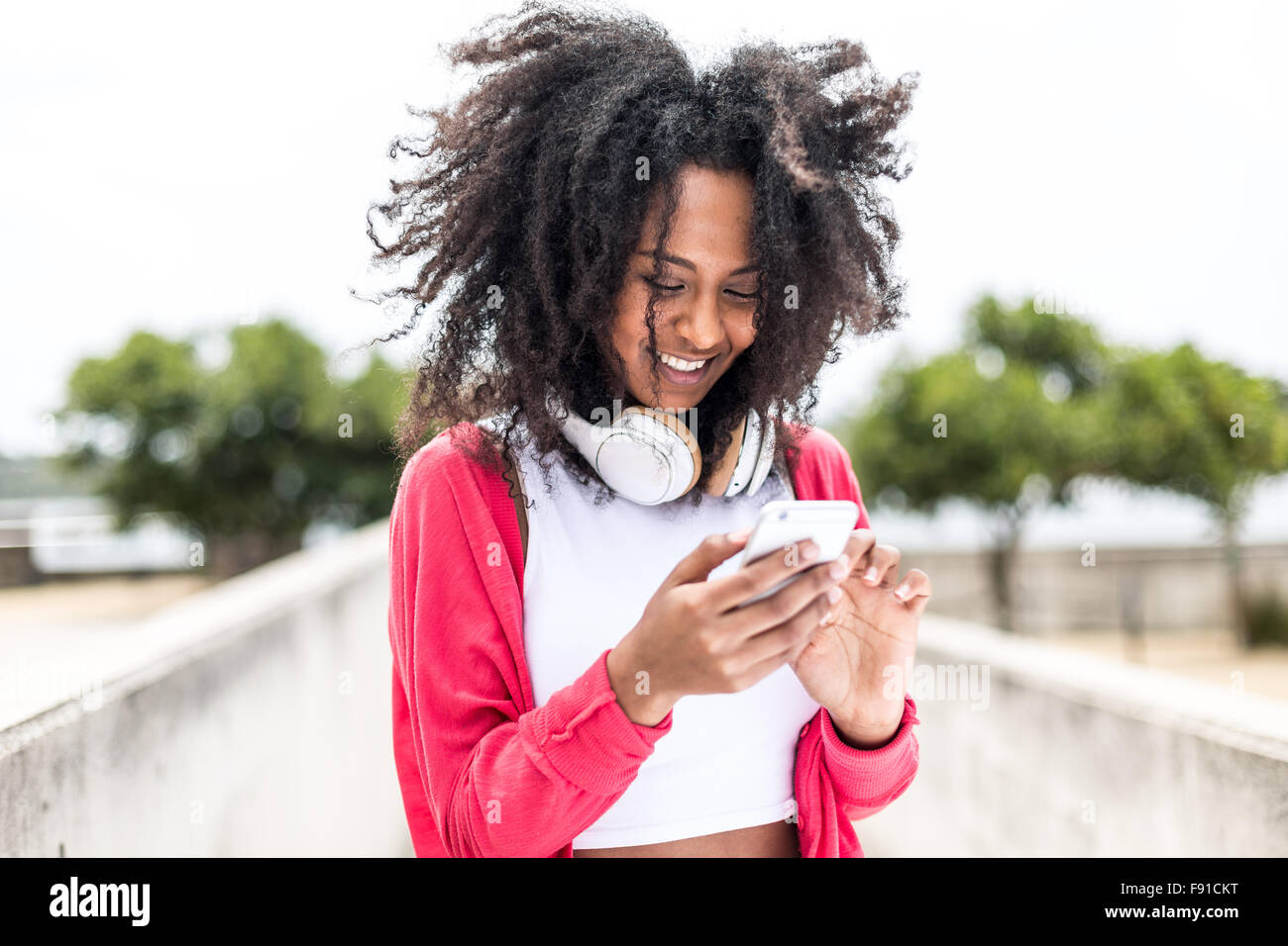 Un giovane di mixed-gara donna ascoltando musica su uno smartphone con le cuffie in un ambiente esterno Foto Stock