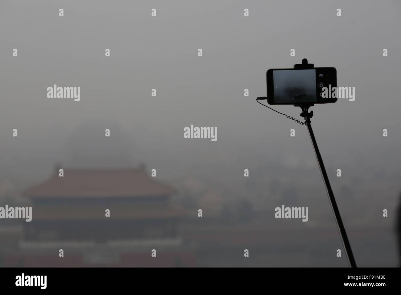 (151213) -- PECHINO, Dic 13, 2015 (Xinhua) -- un turista prende foto della città proibita in mezzo a smog pesante presso il Parco Jingshan a Pechino Capitale della Cina, 8 dicembre, 2015. Sotto un allarme rosso, il più serio a livello, la città di emergenza della sede centrale di gestione consiglia scuole materne, primarie e le scuole superiori di sospendere le classi, vietate le operazioni all'aperto sui siti di costruzione e necessita di alcuni impianti industriali di limitare o di interrompere la produzione. L'uso dell'auto era limitata durante il red alert periodo come le automobili sono ammessi sulle strade a giorni alternati a seconda dei numeri dispari o pari di loro licenza plat Foto Stock