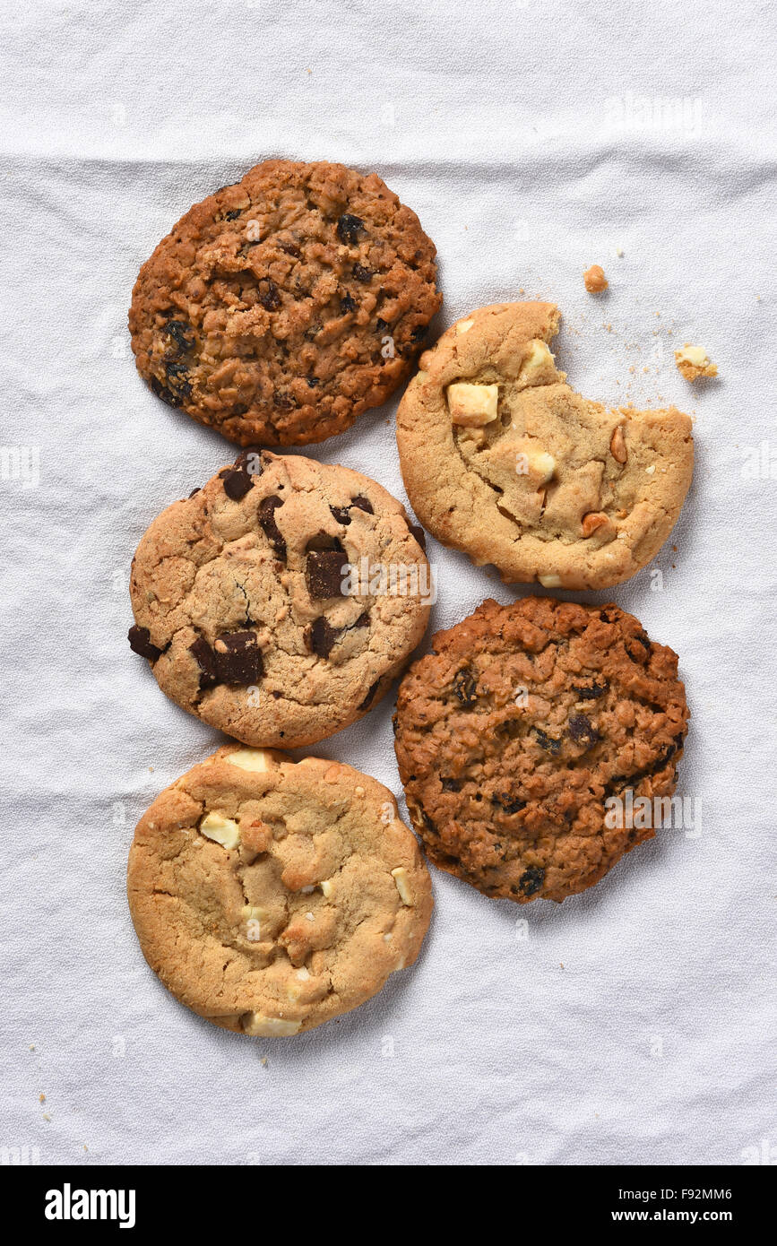Angolo di alta vista di cinque cookies uno con un morso preso fuori di esso. Formato verticale su una cucina bianca asciugamano. Foto Stock