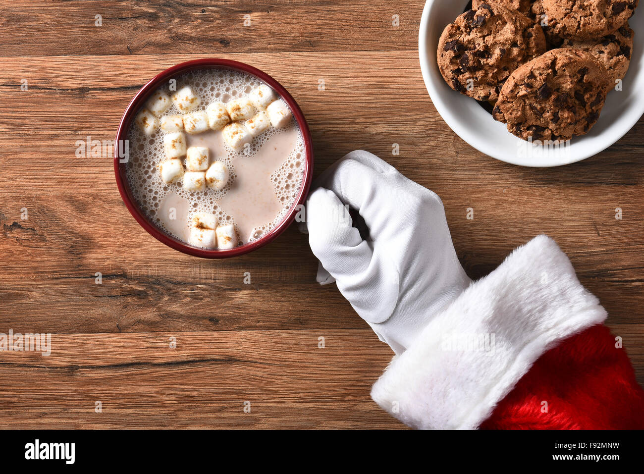 Angolo alto closeup di Santa Claus tenendo una tazza di cioccolata calda su una tavola di legno con la piastra del cookie. Foto Stock