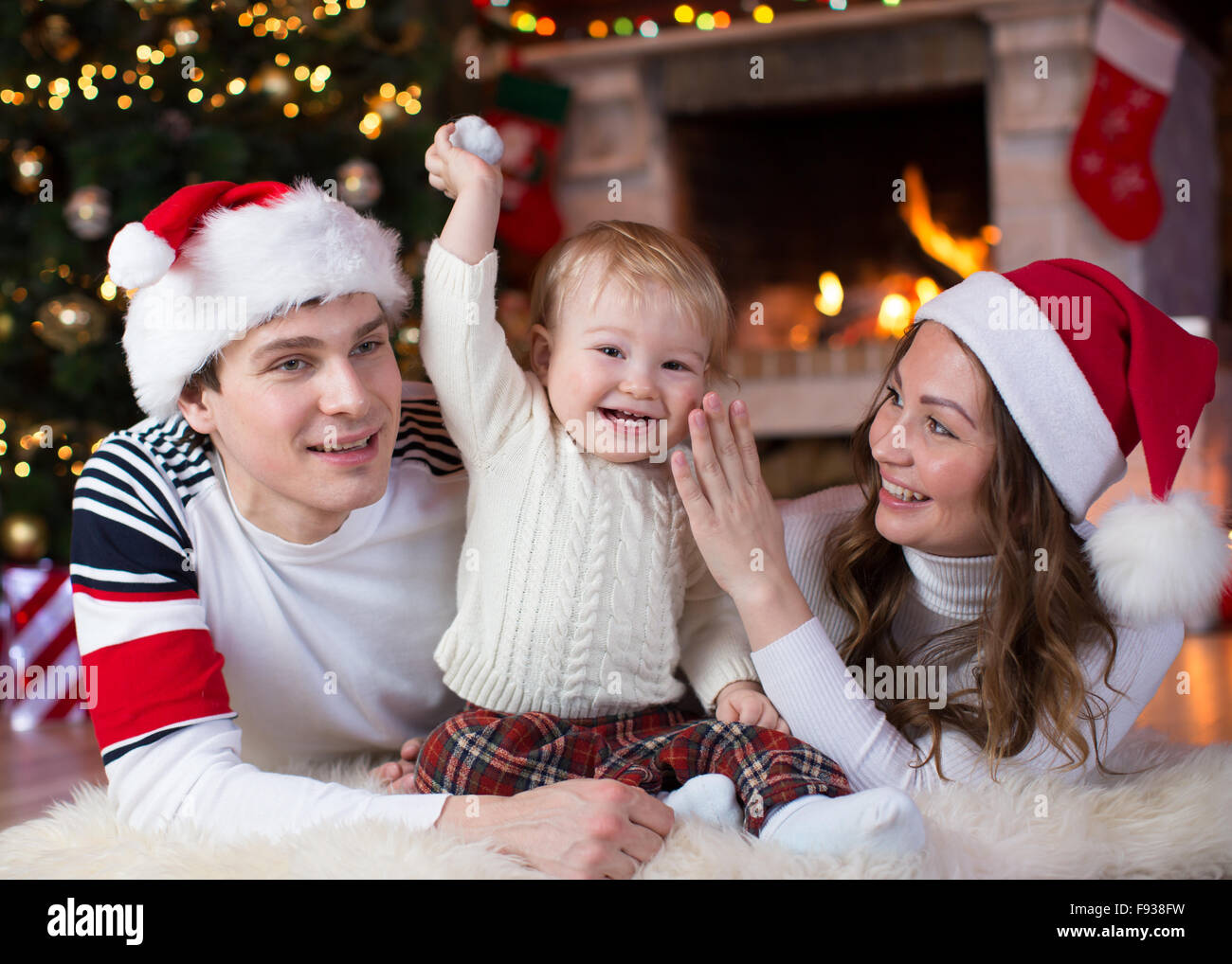 La famiglia felice con il Figlio bambino che giace nei pressi di albero di Natale e caminetto in soggiorno Foto Stock