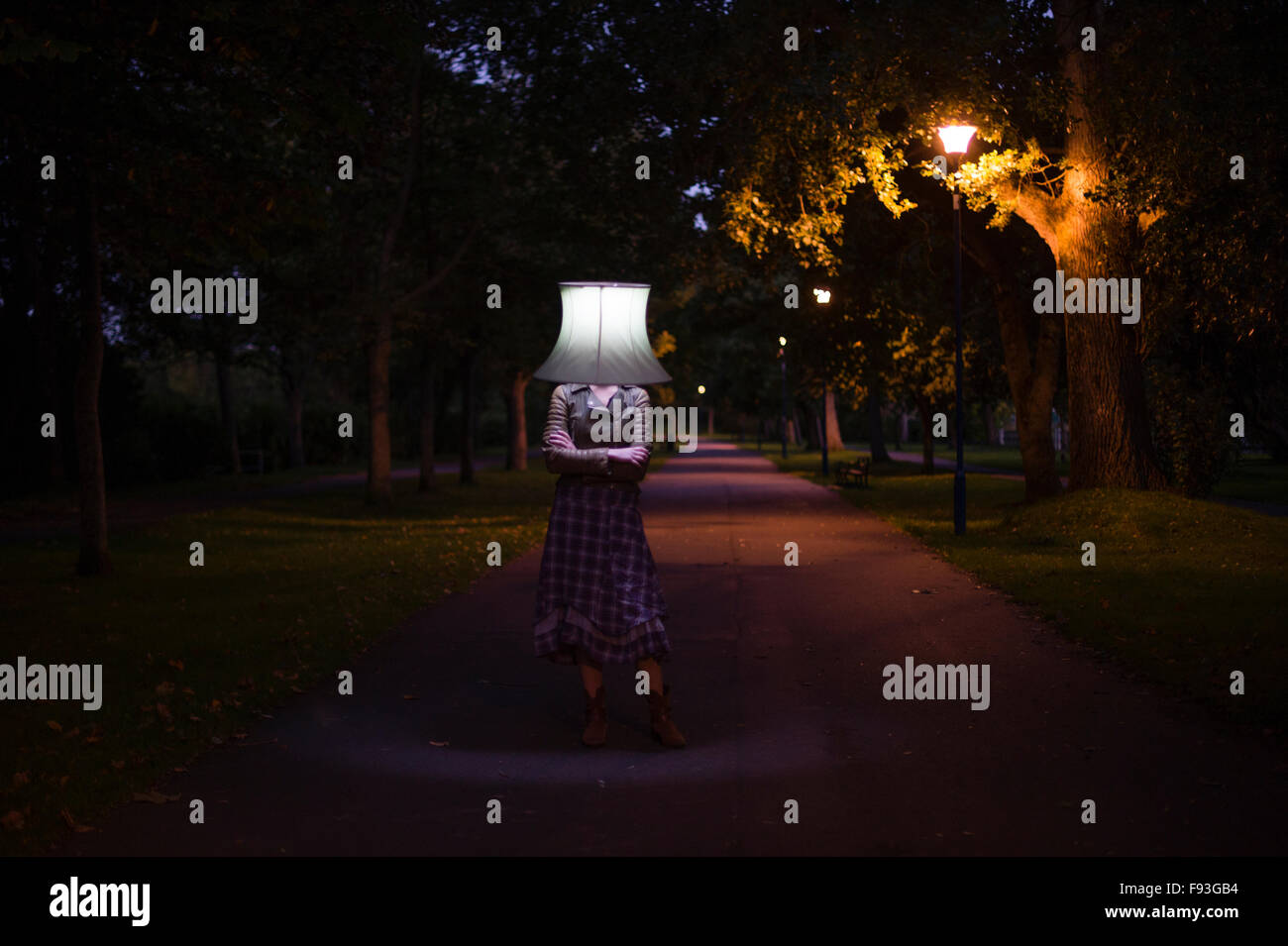 Una donna sola ragazza indossare copricapi dispari: un paralume illuminato sul suo capo all'aperto al crepuscolo Foto Stock