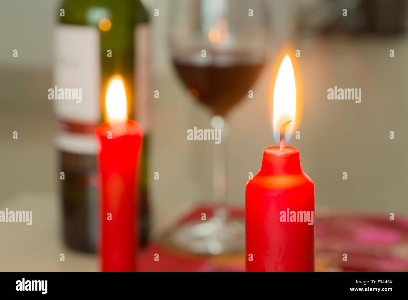Candela rossa e una bottiglia di vino con un bicchiere in background Foto Stock