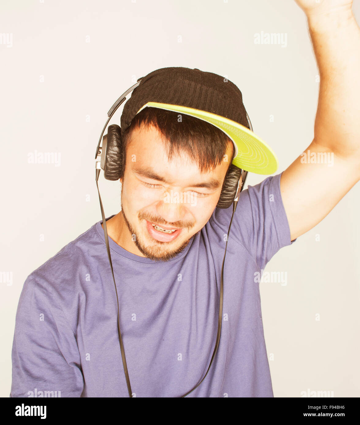 Giovane uomo asiatico in hat e cuffie ascoltando musica su sfondo bianco Foto Stock