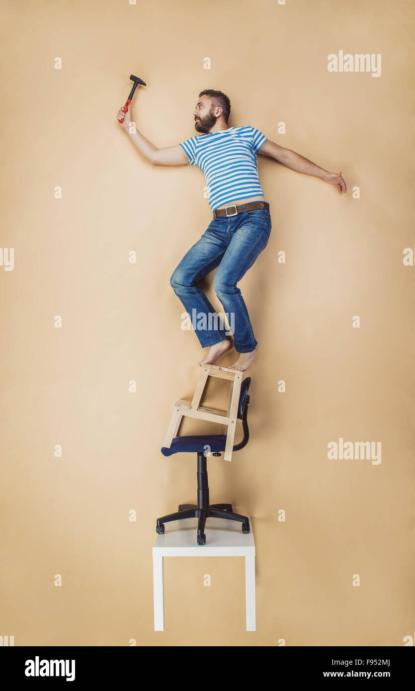 Tuttofare pericolosamente in piedi su una pila di sedie. Studio shot su uno sfondo beige. Foto Stock