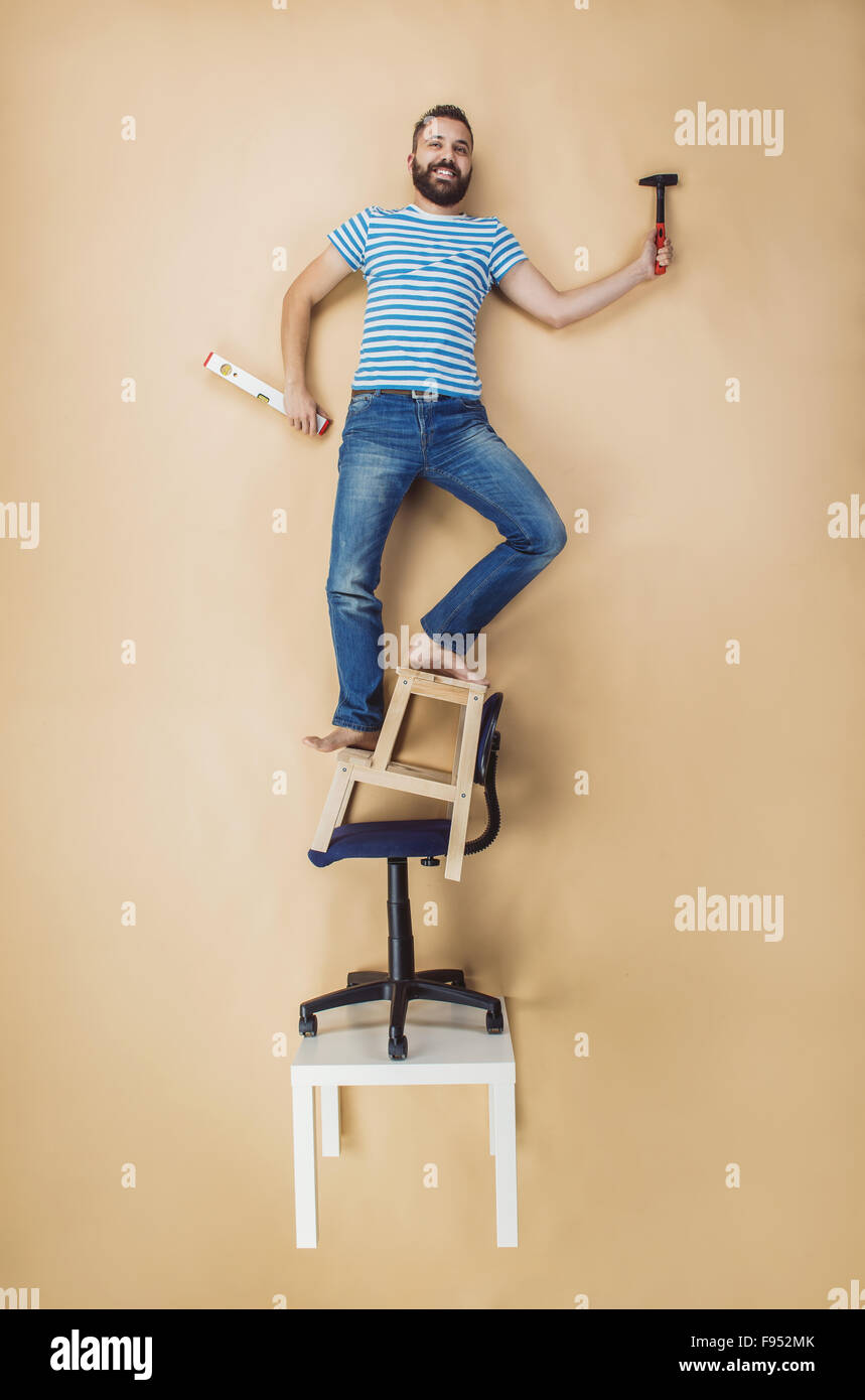 Tuttofare pericolosamente in piedi su una pila di sedie. Studio shot su uno sfondo beige. Foto Stock