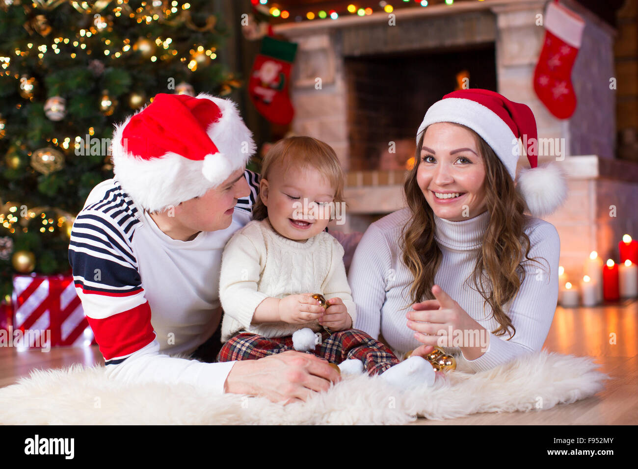 La famiglia felice giocando con il Figlio bambino che giace nei pressi di albero di Natale e caminetto in soggiorno Foto Stock