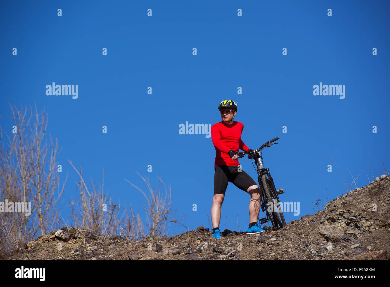 Ciclista uomo in piedi sulla cima di una montagna con la bicicletta e godersi la vista della valle in una giornata di sole contro un cielo blu Foto Stock