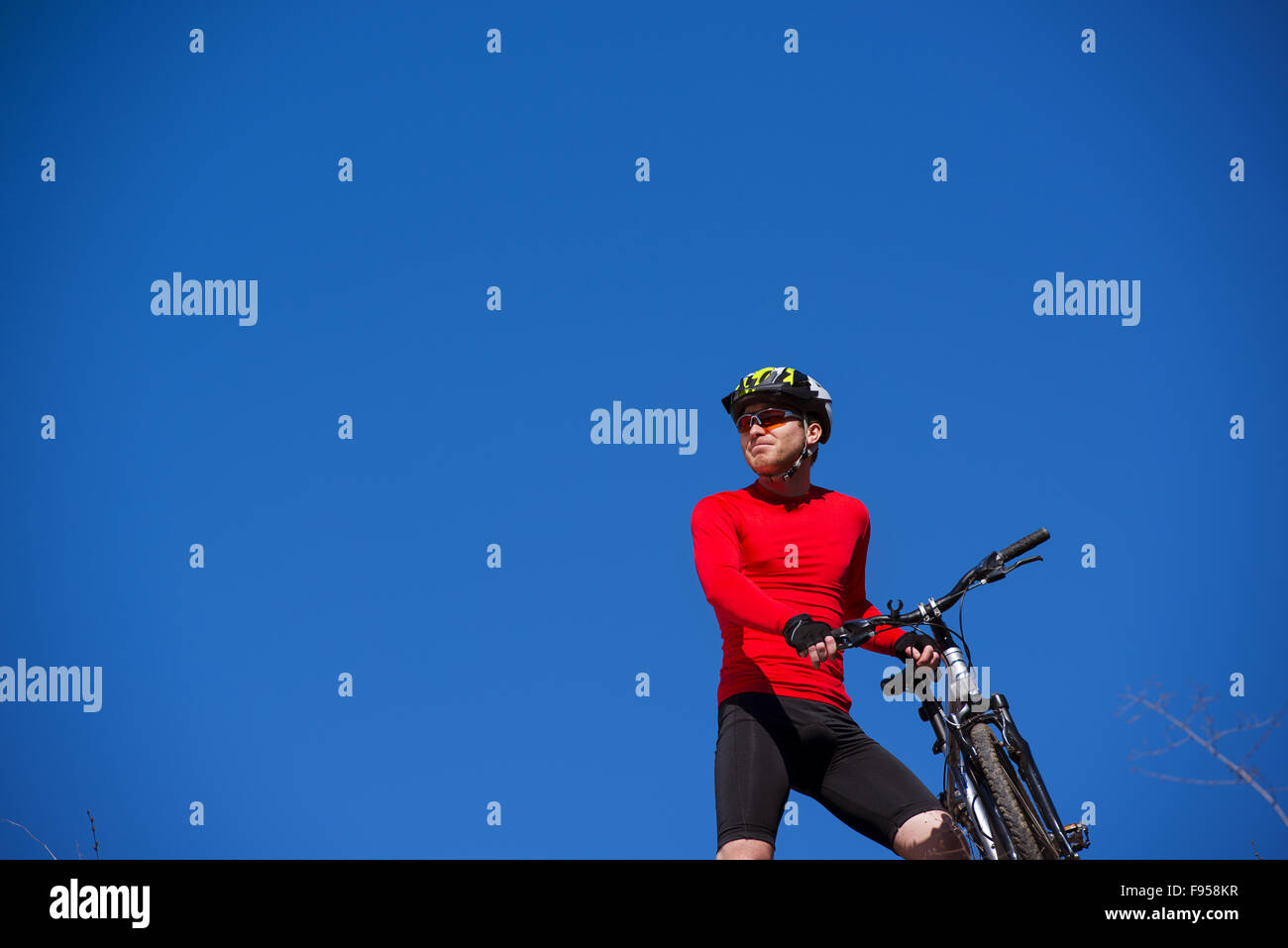 Ciclista uomo in piedi sulla cima di una montagna con la bicicletta e godersi la vista della valle in una giornata di sole contro un cielo blu Foto Stock