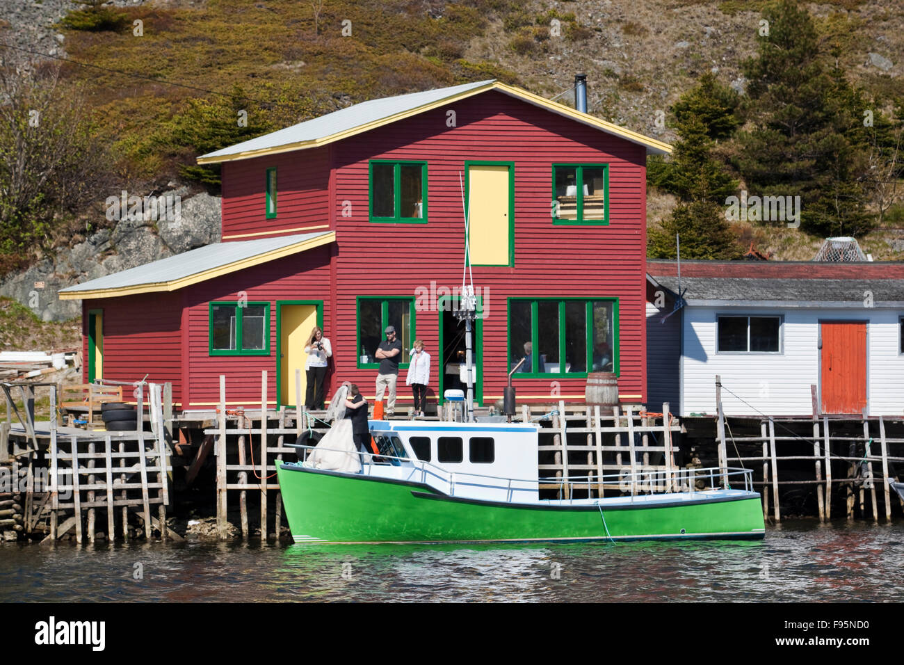Sposi novelli che posano per una foto su un bightly colorate barche da pesca ormeggiate accanto a un capannone di pesca in Quidi Vidi, Terranova, Canada Foto Stock