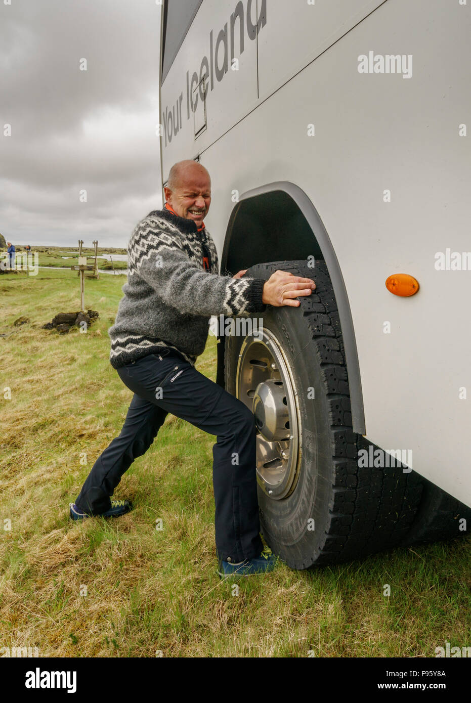 Uomo che cerca di spostare un pneumatico di grandi dimensioni su un tour bus, South Coast, Islanda Foto Stock