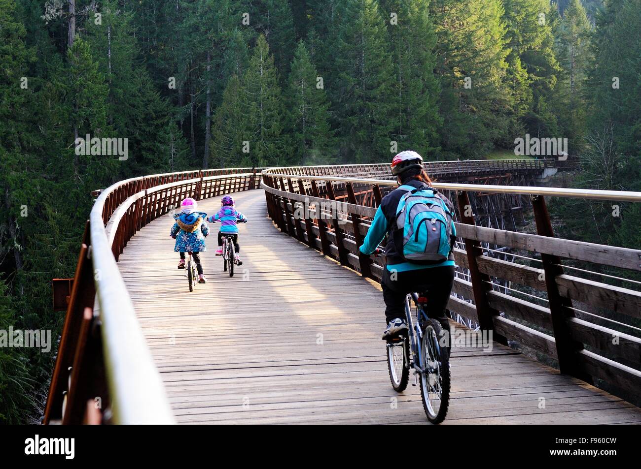 Una donna e i suoi figli in bicicletta attraverso il traliccio Kinsol vicino Lago di Shawnigan, BC. Foto Stock