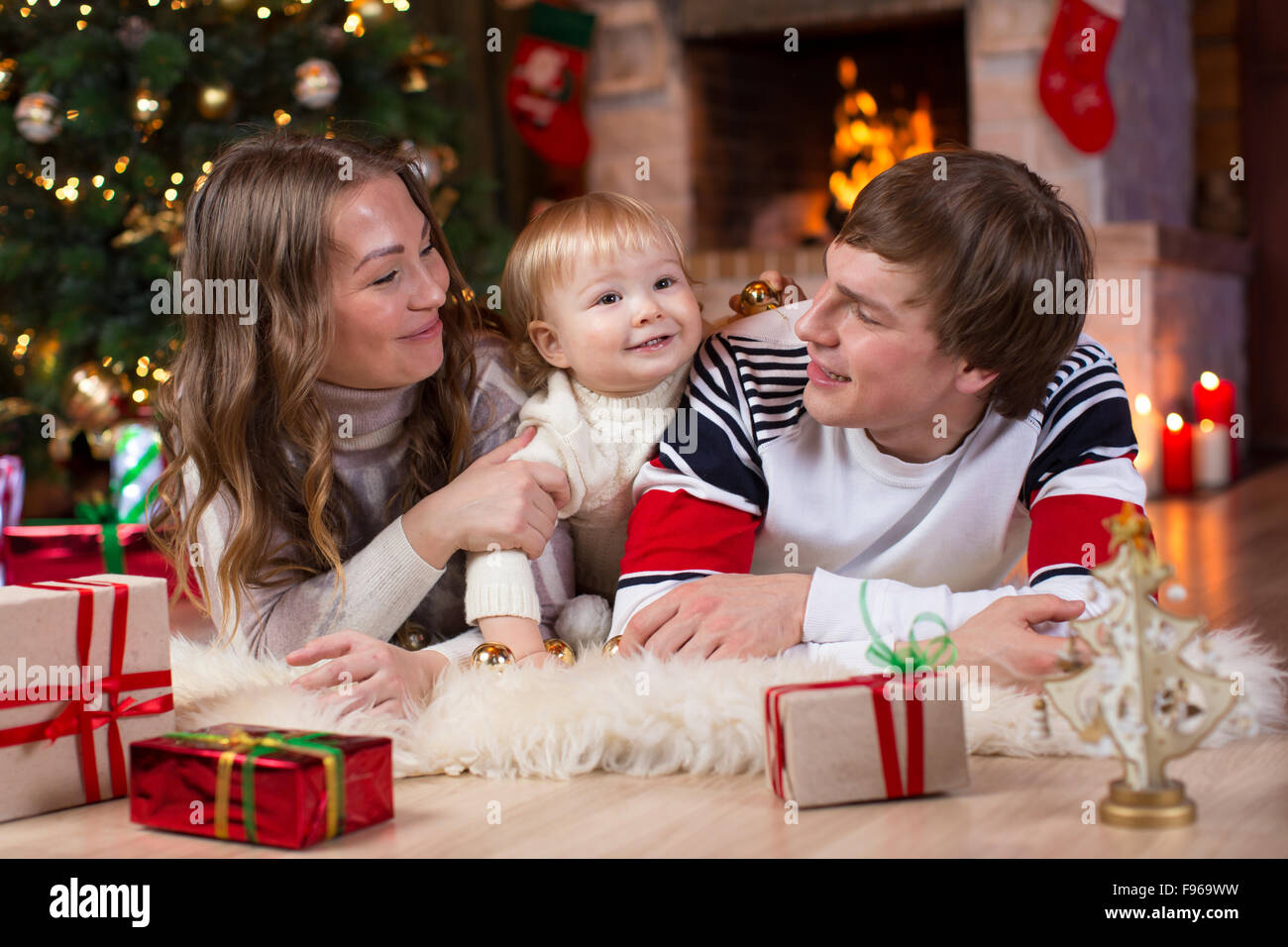 La famiglia felice con il piccolo figlio che giace nei pressi di albero di Natale e caminetto in soggiorno Foto Stock