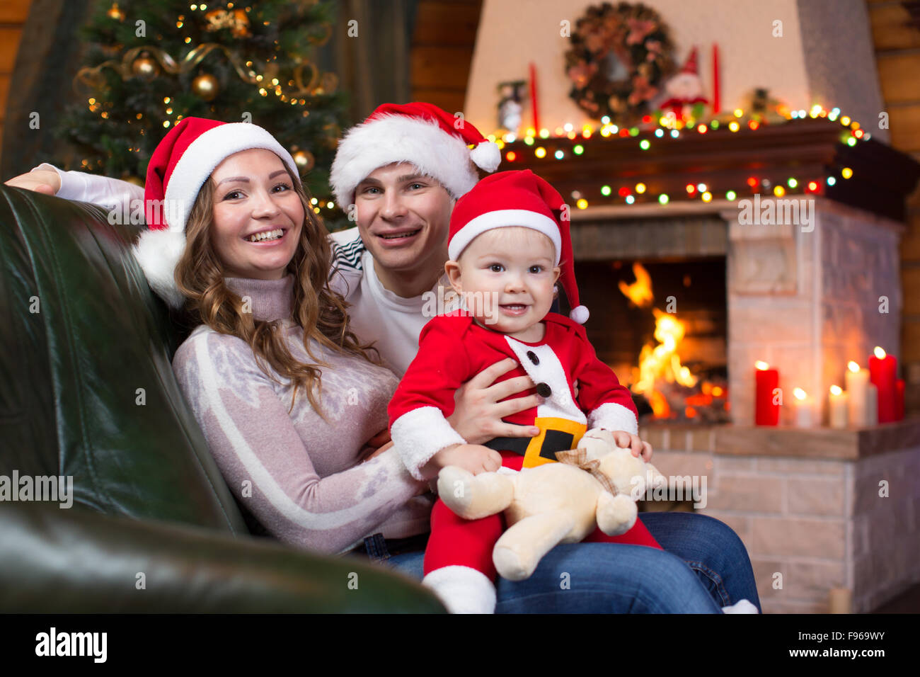 La famiglia felice con il bambino seduto sul divano un divertimento vicino a albero di Natale e caminetto in soggiorno Foto Stock