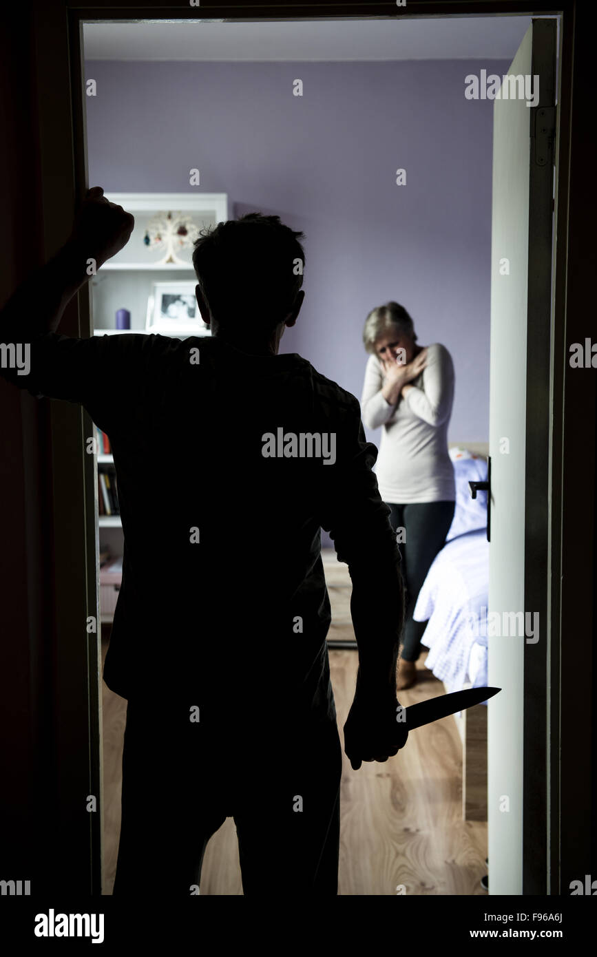 Donna matura in camera da letto è la paura dell'uomo con il coltello. La donna è vittima di violenza domestica e abusi. Foto Stock