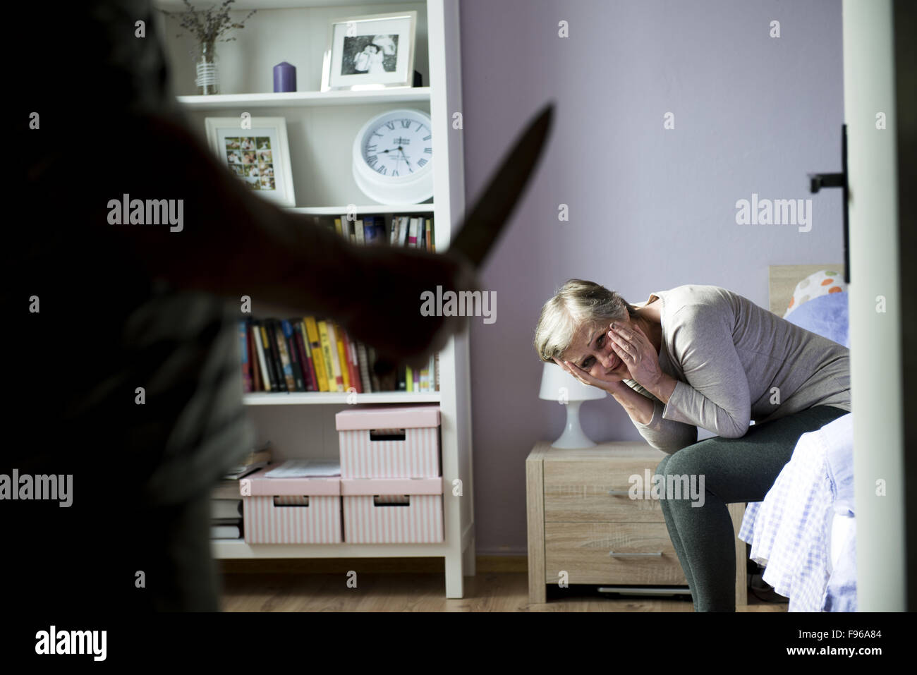 Donna matura siiting sul letto è spaventato da uomo con coltello. La donna è vittima di violenza domestica e abusi. Foto Stock