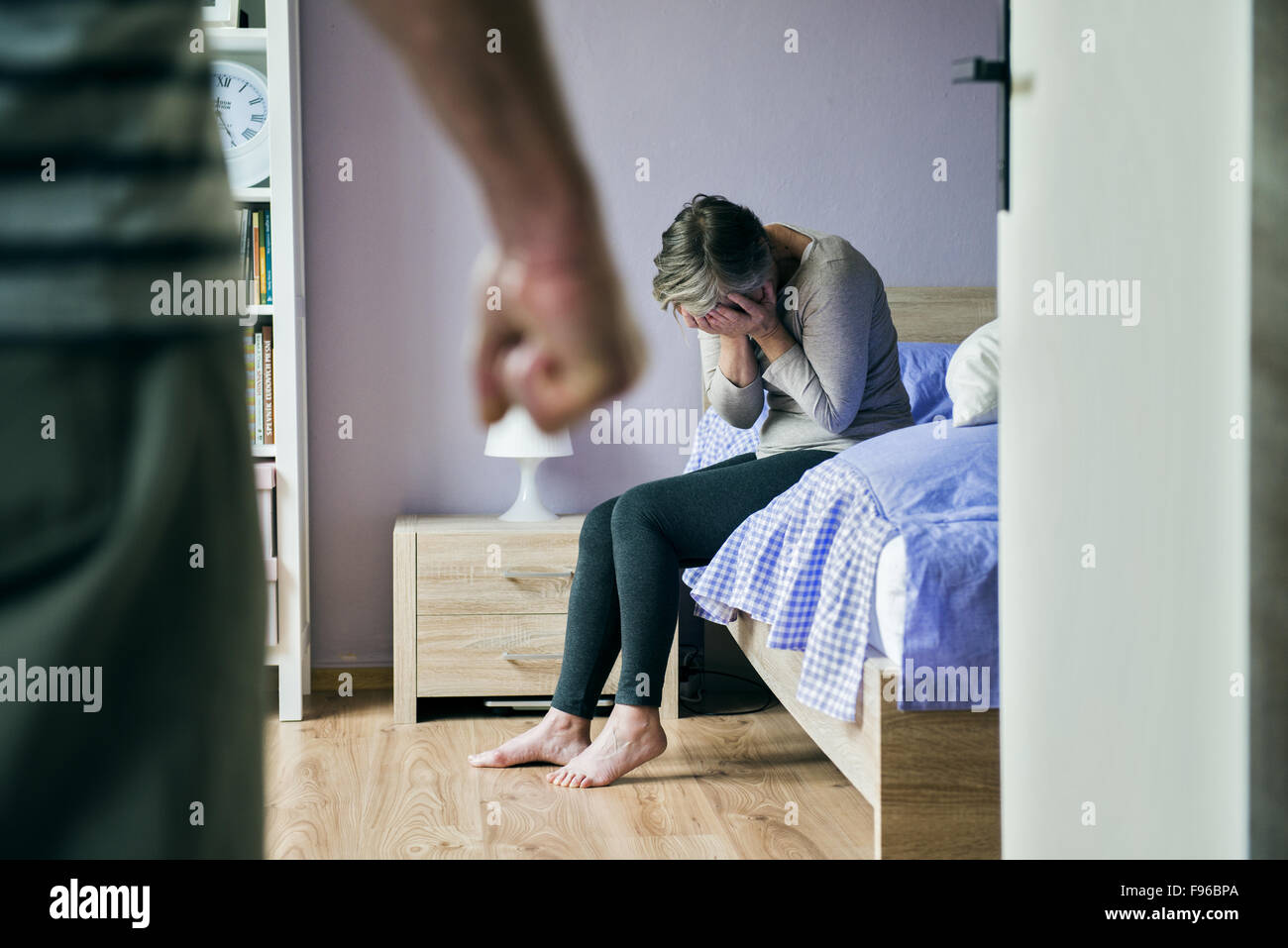 Donna matura seduta sul letto è la paura di un uomo. La donna è vittima di violenza domestica e abusi. Foto Stock
