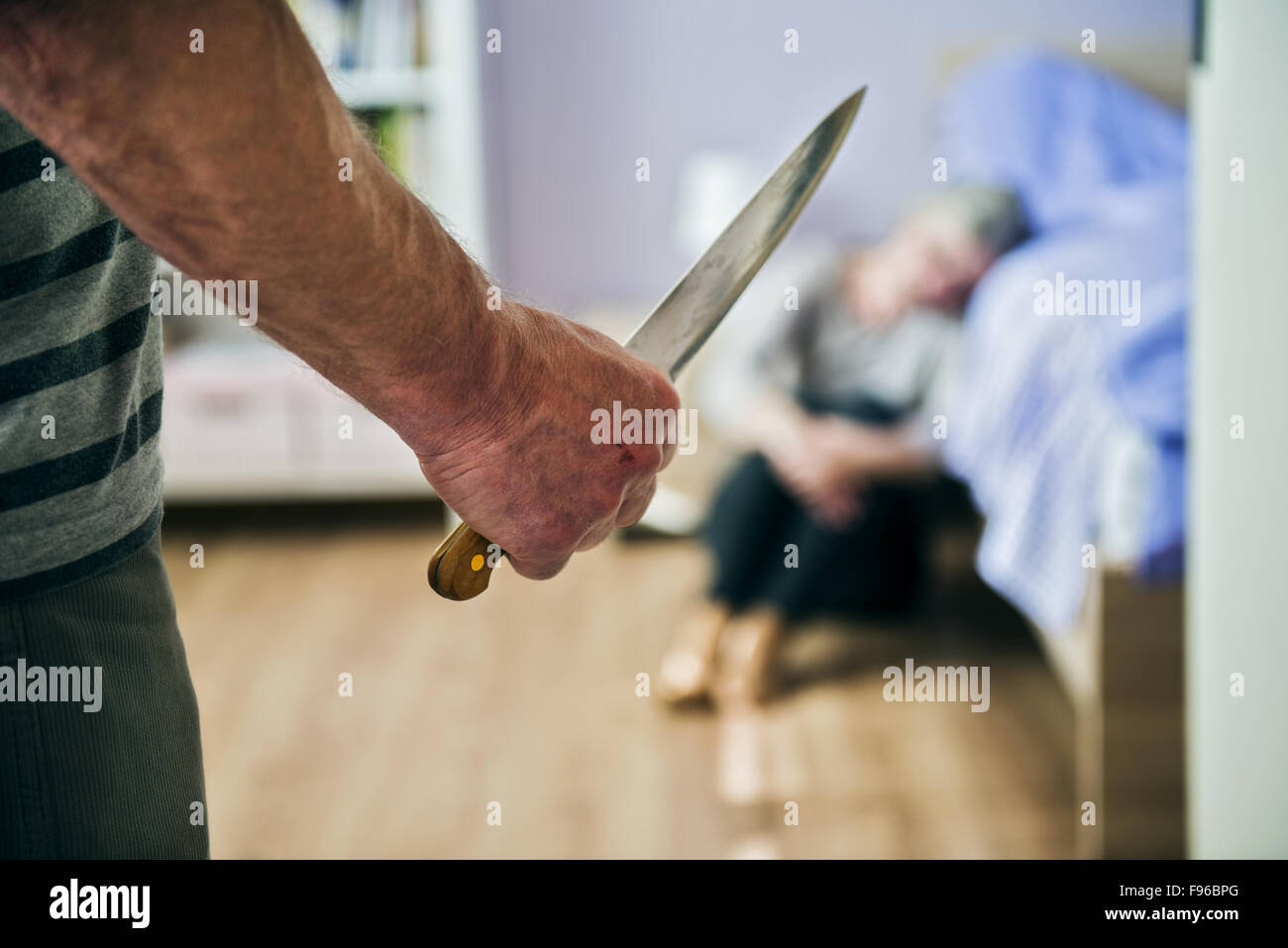 Donna matura seduta sul pavimento è spaventato da uomo con coltello. La donna è vittima di violenza domestica e abusi. Foto Stock