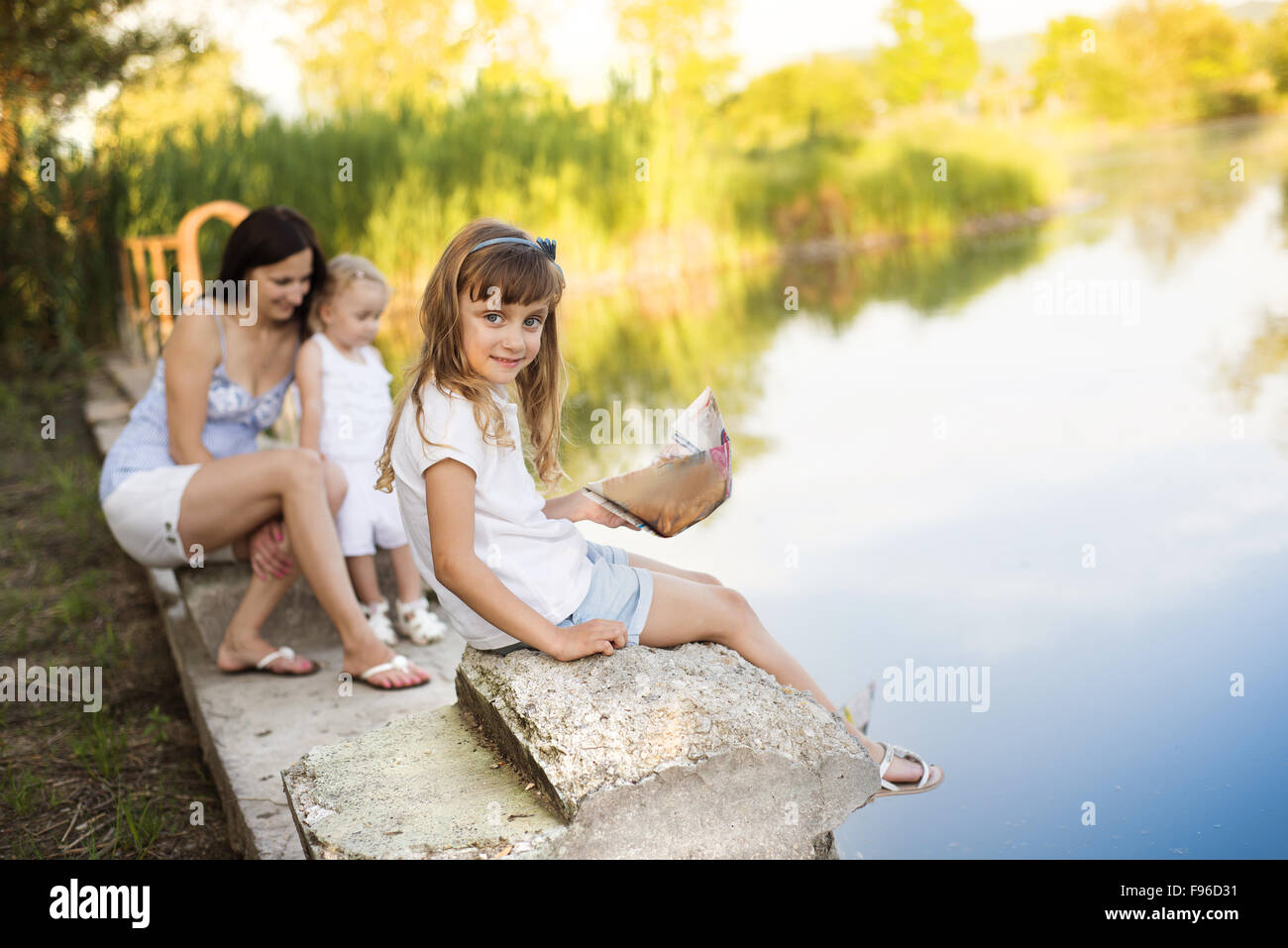 Due piccole sorelle e la loro mamma giocando con la carta barche sul lago Foto Stock