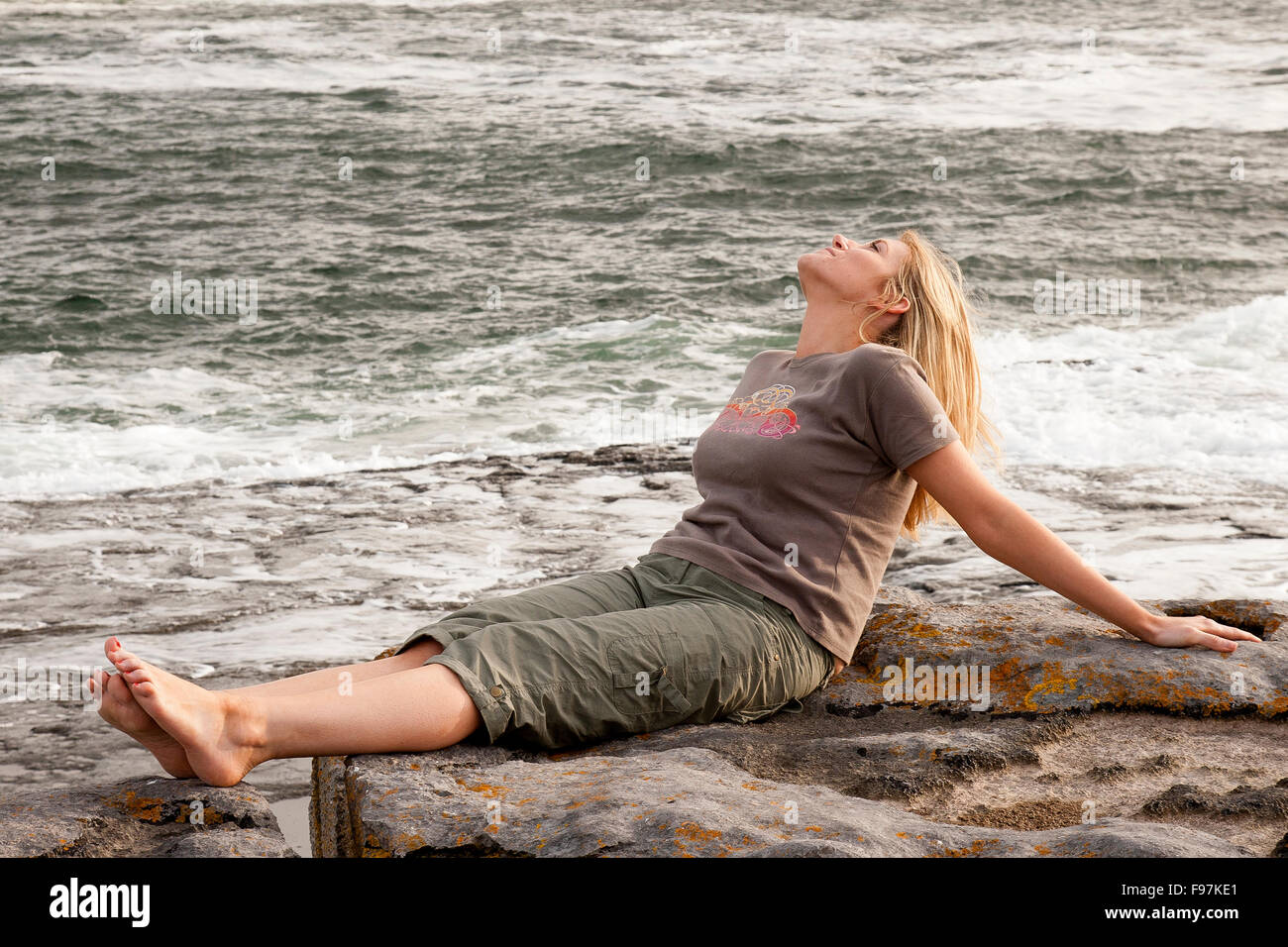 Giovane donna seduta sulla riva del mare, Doolin punto, County Clare, Irlanda Foto Stock