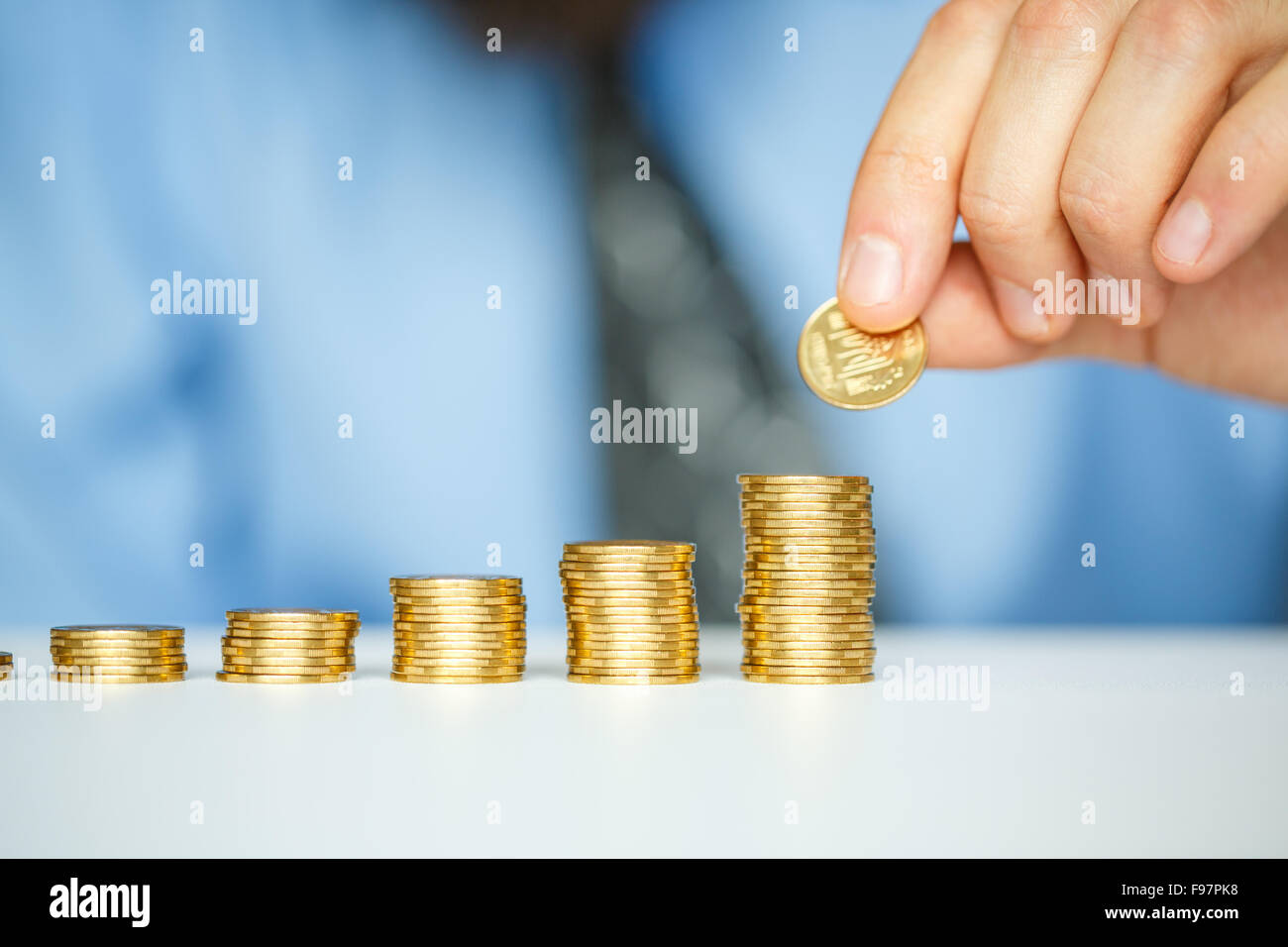 Risparmio di mano maschio di impilamento delle monete in oro in colonne crescente Foto Stock