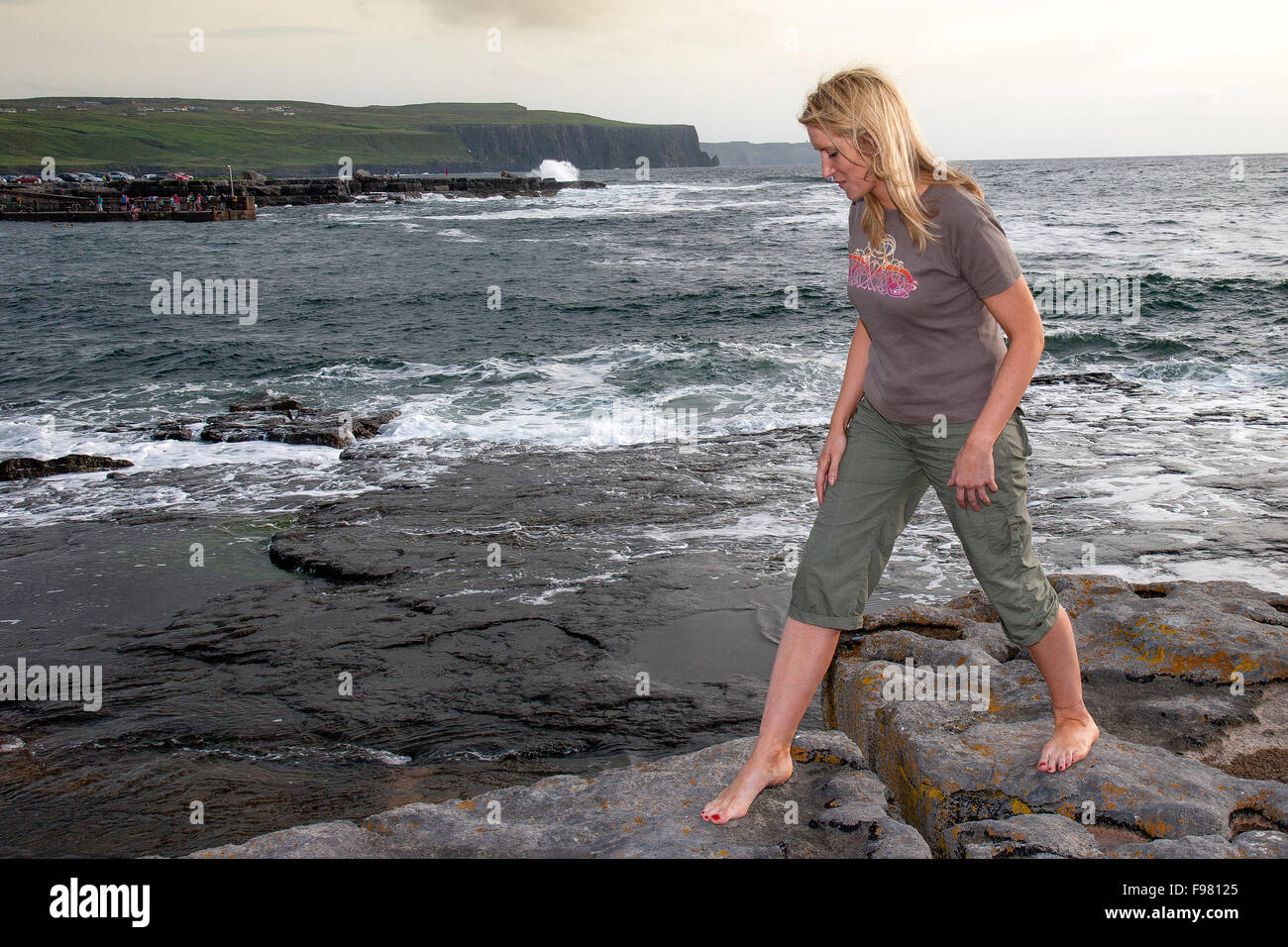 Giovane donna seduta sulla riva del mare, Doolin punto, County Clare, Irlanda Foto Stock