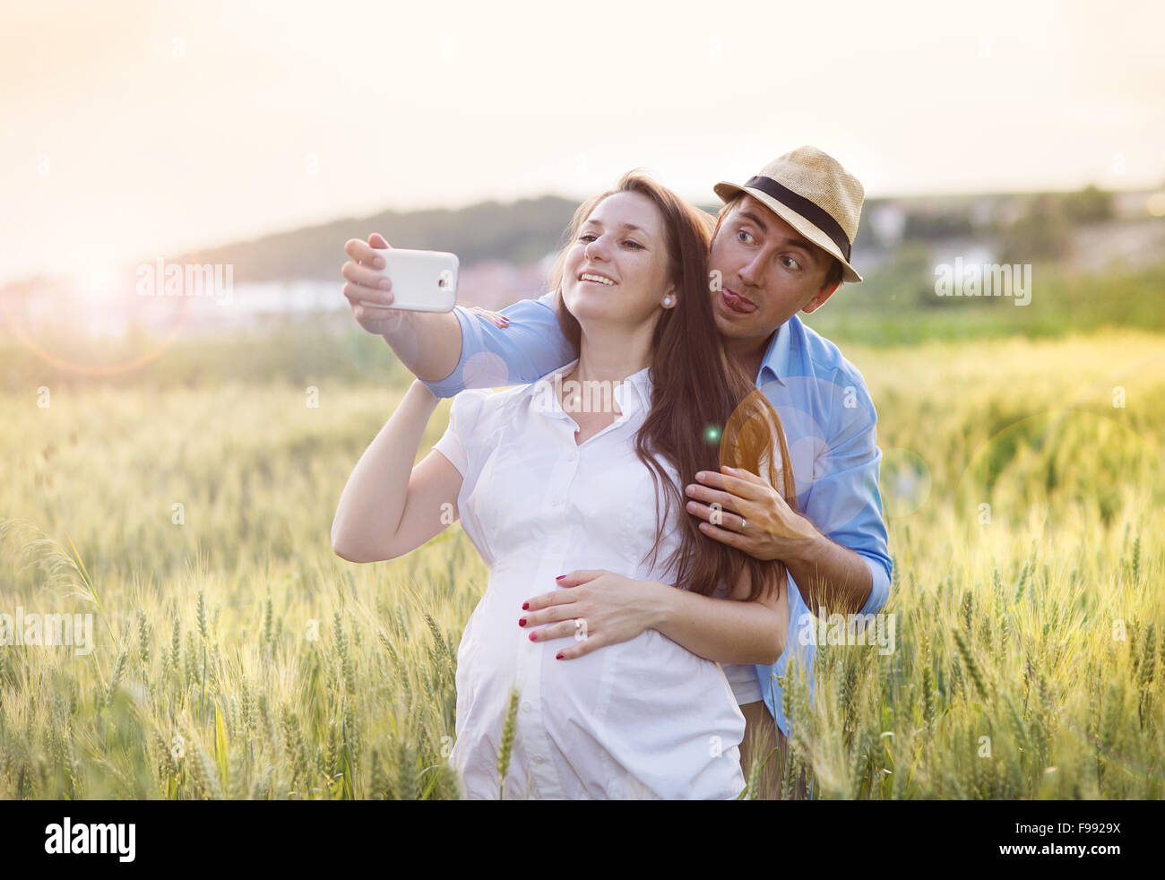 Felice giovane incinta giovane costeggiata in natura e prendendo selfie Foto Stock