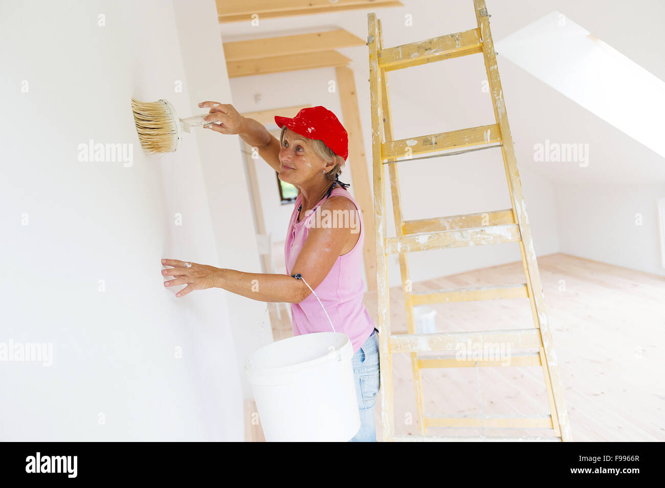 Senior donna pittura parete nella nuova casa. Ella è utilizzando la scala. Foto Stock